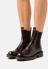 Bottes de cheville en cuir brun foncé avec une texture crocodile, des panneaux latéraux élastiques et une semelle robuste pour une meilleure adhérence.