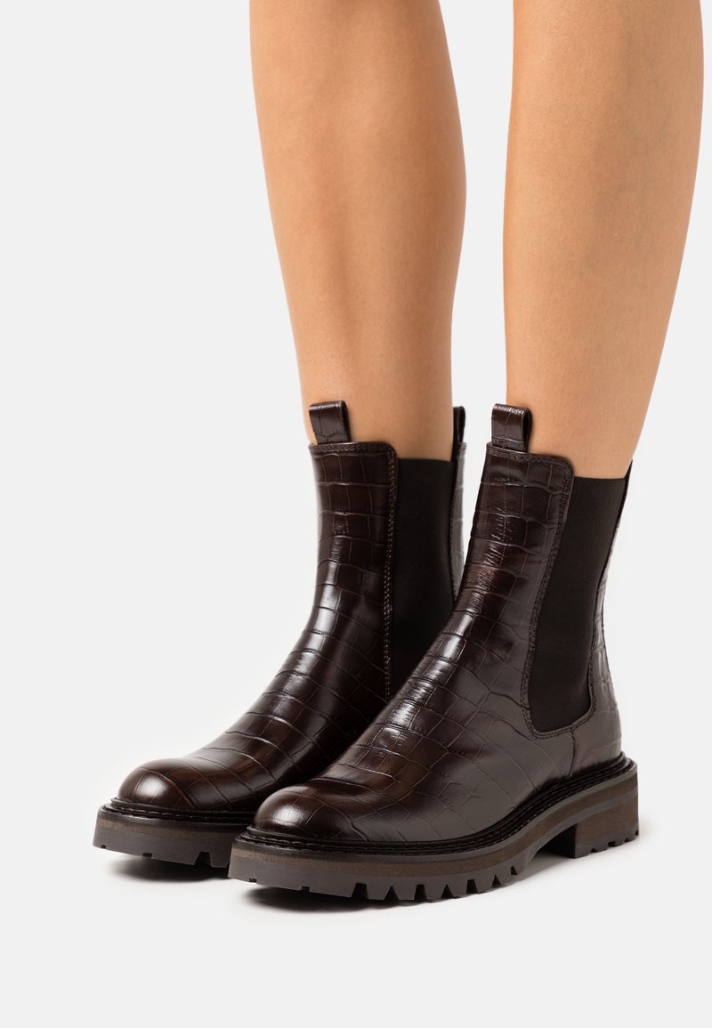 Bottes de cheville en cuir brun foncé avec une texture crocodile, des panneaux latéraux élastiques et une semelle robuste pour une meilleure adhérence.