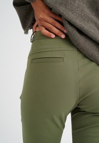 Pantaloni verde oliva su misura realizzati in materiale elastico, dotati di una tasca posteriore e una superficie liscia con cuciture dettagliate.