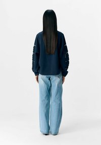 Marineblauwe sweatshirt met gestructureerde accenten op de mouwen, gecombineerd met lichtblauwe hoge taille jeans met brede pijpen. Glad materiaal met een ontspannen pasvorm.