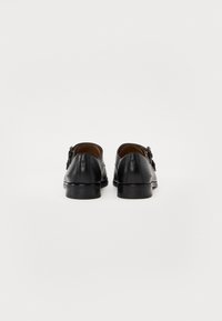 Black leather shoes with a smooth finish, featuring a rounded toe and decorative tassel accents, set on a low black sole.