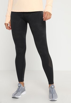 Sorte leggings med et struktureret mønster, der har mesh-detaljer på siderne. Sammen med lysegrå træningssko.