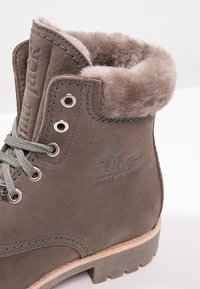 Botine din suede gri, cu căptușeală din blană sintetică, ochiuri metalice și șirete gri. Dispun de un logo embosat și o cusătură în contrast pe partea superioară.