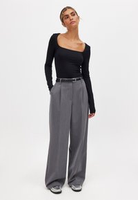 Top nero a maniche lunghe con scollatura asimmetrica, abbinato a pantaloni grigi a vita alta e gamba larga, con scarpe con accenti argentati.