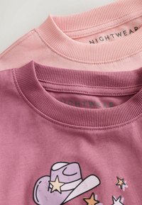 Dwie bluzy z okrągłym dekoltem w kolorze różowym i mauve, z prążkowanymi kołnierzami oraz graficznym wzorem kapelusza kowbojskiego z gwiazdami na bluzie mauve.