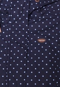 Navy blue coat with light blue polka dots, featuring a zip closure, two front pockets, and a sewn label with brand name.