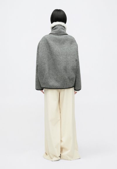 Siva jakna od vune s visokom ovratnikom, ukrašena bijelim umjetnim krznom. Uparen s laganim bež hlačama širokih nogavica.