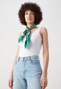 Green patterned silk scarf tied around the neck, paired with a white tank top and light blue high-waisted jeans.
