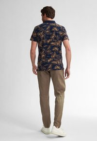 Mörkblå kortärmad skjorta med ett blommigt guldmönster, i kombination med ljusbruna byxor och vita sneakers, som visar en avslappnad passform och en avslappnad design.