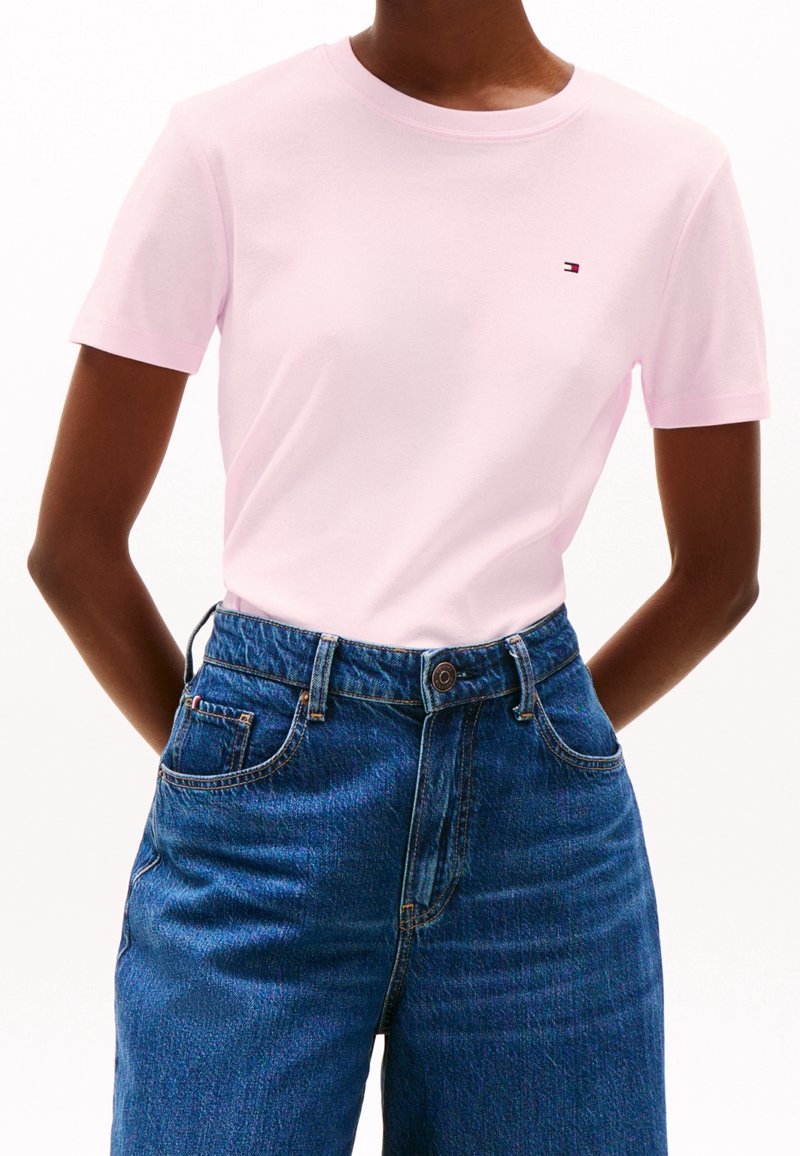 Světle růžové tričko s krátkým rukávem z bavlny, s kulatým výstřihem a malým logem. Slučuje se s džíny z modrého denimu s vysokým pasem.