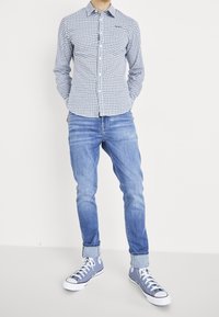 Blauw-wit geruit overhemd met knopen, lichtblauwe spijkerbroek en blauwe sneakers met hoge schacht en witte zolen. Casual outfit met een ontspannen pasvorm.