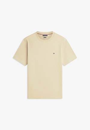Beżowy T-shirt z krótkim rękawem i okrągłym dekoltem, z małym logo Tommy Hilfiger na lewej piersi, ułożony na płasko na białym tle.