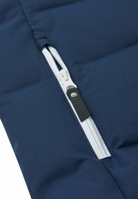 Marinefarbene Stofftasche mit einem weißen Reißverschluss, ausgestattet mit einem schwarzen Leder-Zipper. Die Textur ist weich, mit einer glatten Oberfläche und gepolstertem Design.
