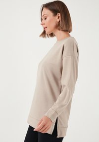 Felpa a maniche lunghe color beige chiaro con scollatura rotonda, fessure laterali all'orlo e polsini a costine, realizzata in un tessuto liscio.