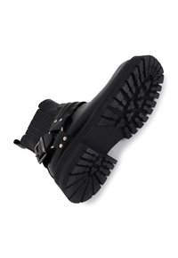 Botín negro hasta el tobillo con un upper de cuero suave, una banda elástica ancha y una suela de goma gruesa y texturizada con patrones de relieve profundos.