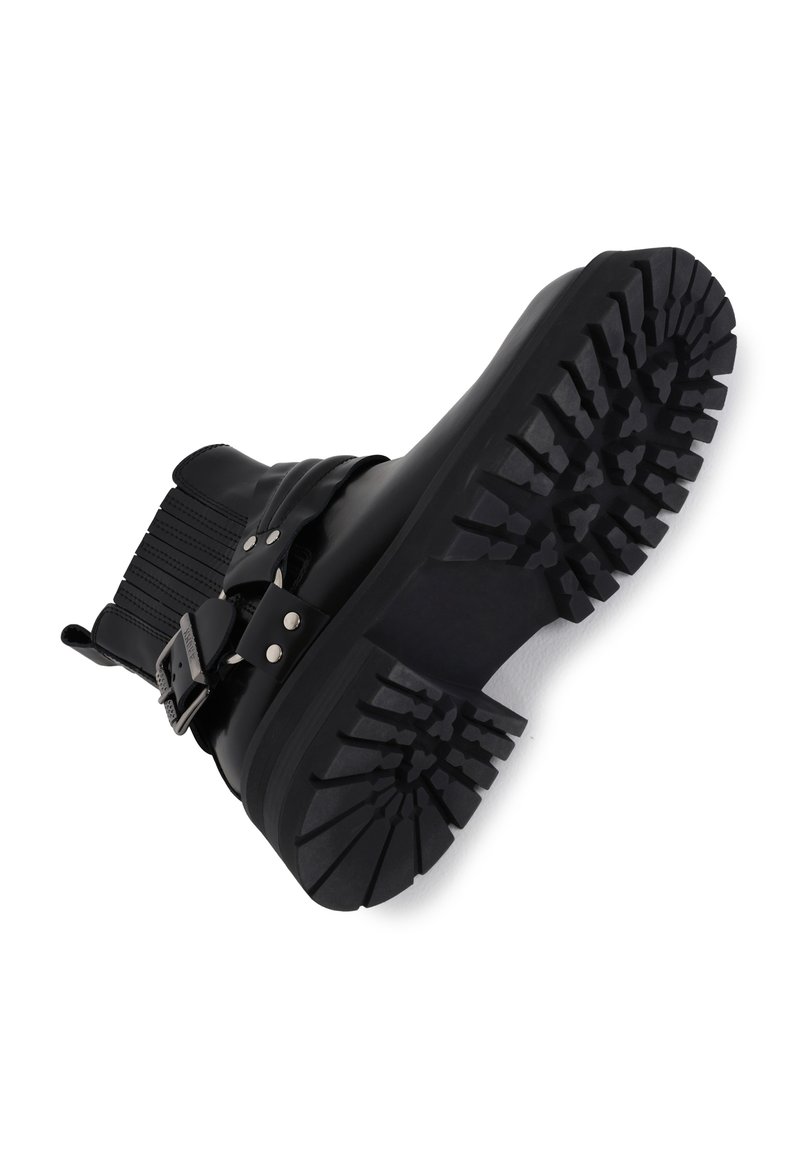 Schwarze Knöchelschuhe aus glattem Leder, mit einem breiten elastischen Band und einer klobigen, strukturierten Gummisohle mit tiefen Profilmustern.