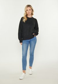 Pulover negru tricotat cu model, cu guler rotund, asortat cu blugi skinny albaștri și adidași albi. Textură moale, croială lejeră și manșete cu nervuri.