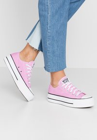 Rosa canvas sneakers med vita gummisulor, svarta ränder och vita snören. Designen har en låg silhuett och rundad tå.