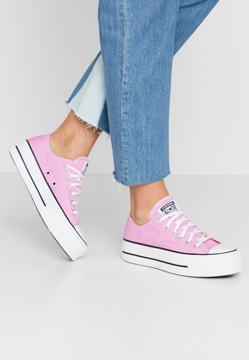 Rosa canvas sneakers med vita gummisulor, svarta ränder och vita snören. Designen har en låg silhuett och rundad tå.