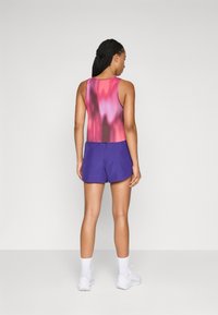 Top justo sem mangas com degradê em rosa e roxo, combinado com calções roxos soltos. Meias e sapatilhas brancas completam o visual atlético.