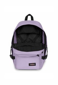 Mochila púrpura con interior negro, compartimento principal con cremallera, correas ajustables y bolsillo frontal con parche de logo. Textura de tela suave.