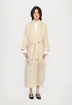 Beige linen robe with embroidered palm tree design in dark red, featuring a belted waist and wide sleeves, layered over a white shirt.