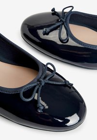 Navy patentoim matto ballet-tossut, joissa on pyöristetty kärki, joustava reunus ja koristeellinen nauhadetail. Tasainen pinta ja pehmeä sisävuori.