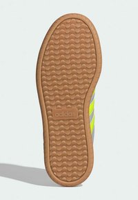 Shoe sole featuring textured rubber in tan with a wavy pattern, displaying three bright yellow stripes and an embossed "adidas" logo.