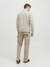 Beige Zip-Neck-Sweatshirt mit hohem Kragen, kombiniert mit hellbeigen Cargo-Hosen mit mehreren Taschen und schwarzen Slippers.