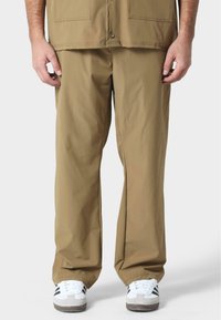 Pantalones de pierna ancha en color caqui con una textura suave y dos grandes bolsillos frontales, combinados con zapatillas blancas con detalles en negro.