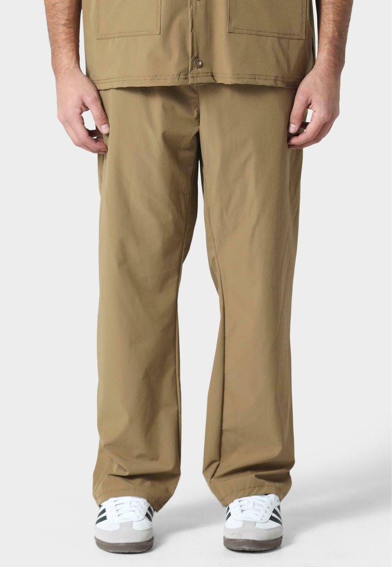 Pantalones de pierna ancha en color caqui con una textura suave y dos grandes bolsillos frontales, combinados con zapatillas blancas con detalles en negro.