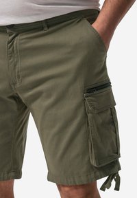 Pantaloni cargo verde oliva con tasche laterali, una tasca con zip e coulisse regolabile all'orlo. Realizzati in un tessuto morbido e resistente.