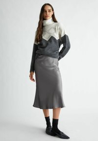 Maglione grigio e bianco a collo alto con dettagli a motivo geometrico, abbinato a una gonna midi in satin grigio liscia e scarpe nere con decorazioni.