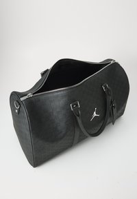 Mustat duffel-reput valmistettu teksturoidusta nahasta. Varustettu hopeisilla yksityiskohdilla, ylhäältä avautuvalla vetoketjulla ja Jordan-logo näkyvästi esitetyllä edessä.