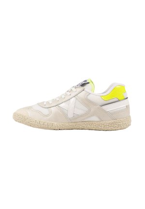 Zapatilla baja blanca y beige con suela texturizada, detalles de malla blanca y un acento amarillo brillante en el cuello del talón.