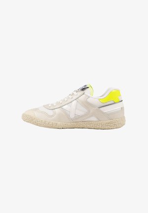 Zapatilla baja blanca y beige con suela texturizada, detalles de malla blanca y un acento amarillo brillante en el cuello del talón.