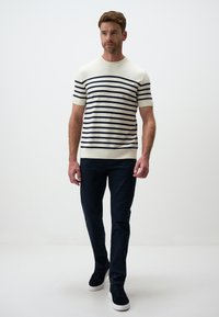 Koszulka z krótkimi rękawami w kolorze kremowym, dzianinowa, w granatowe paski, połączona z granatowymi spodniami i ciemnymi sneakersami, z prostym okrągłym dekoltem i dopasowanym fasonem.