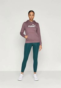 Sweatshirt capuz cor bordo com logotipo branco, combinado com leggings azul-turquesa e sapatilhas brancas, apresentado por um modelo contra um fundo neutro.