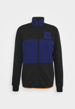 Czarna i granatowa kurtka z polaru z pełnym zamkiem błyskawicznym, stójką, długimi rękawami, logo Adidas na lewej piersi oraz pomarańczowym obszyciem na dole.