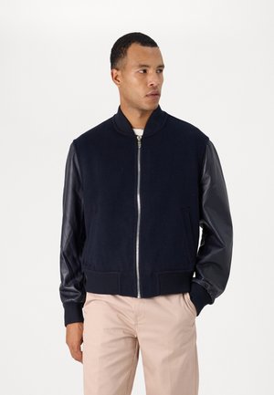 Navy bomber jacket with wool body and leather sleeves, featuring a zip front, ribbed cuffs, and two front pockets. Simple and modern design.