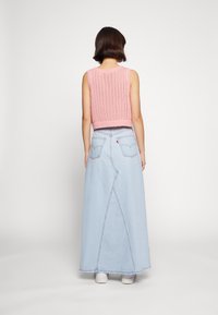Haut sans manches en tricot rose avec un motif texturé, associé à une longue jupe en jean bleu clair avec des coutures contrastées et deux poches arrière.