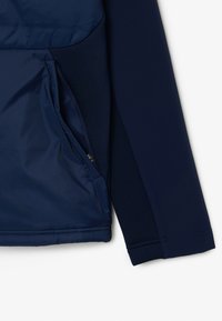 Maglia a maniche lunghe blu navy in tessuto testurizzato, con una tasca con zip sul davanti e un pannello liscio a contrasto sul petto.