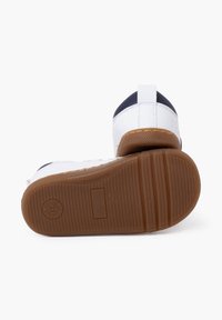 Scarpe per bambini bianche e blu navy con una suola in gomma testurizzata, che mostra un leggero tacco e un dispositivo di estrazione sul retro per facilitare l'indossamento.