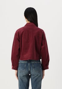 Bourgogne cropped corduroy jakke med knappede ærmer, parret med højtaljede lyseblå denim jeans med baglommer.