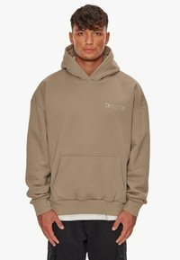 Beige Kapuzenpullover aus weichem Stoff, mit einer Kängurutasche, Kordelzug-Kapuze und dezentem Logo in der oberen linken Ecke.
