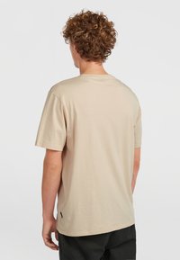 T-shirt in cotone beige con maniche corte, collo rotondo e un sottile etichetta sulla cucitura laterale. Texture liscia, vestibilità casual.