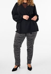 Top nero avvolgente con maniche lunghe e un fiocco in vita, abbinato a pantaloni grigio a strisce di zebra. Scarpe nere con tacco alto completano il look.