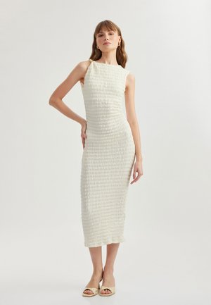 White, fitted midi dress with textured fabric. Features a modest neckline and shoulder detailing, paired with beige open-toe heels.