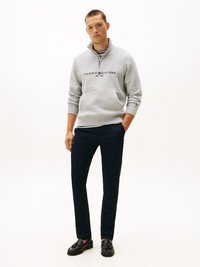 Pullover in pile grigio con mezzo zip, con logo "TOMMY HILFIGER EST. 1985" in navy. Abbinato a pantaloni blu scuro e mocassini neri.