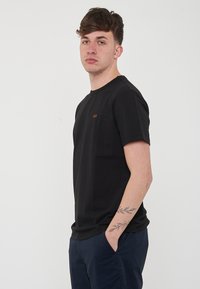 T-shirt nera a maniche corte realizzata in cotone morbido, con scollatura rotonda e un piccolo logo arancione sul petto.